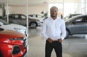 retrato do bonito africano americano vendedor às local de trabalho dentro carro sala de exposições foto