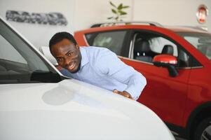 Novo carro proprietário. feliz africano americano homem tocante abraçando dele novo em folha auto foto