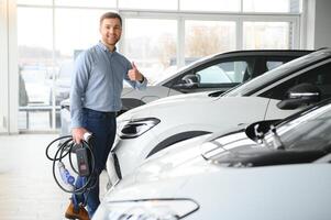 jovem homem, vendendo elétrico carros dentro a showroom. conceito do comprando ecológico carro para família foto