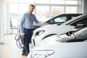 jovem homem, vendendo elétrico carros dentro a showroom. conceito do comprando ecológico carro para família foto