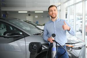 jovem homem, vendendo elétrico carros dentro a showroom. conceito do comprando ecológico carro para família foto