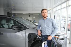 jovem homem, vendendo elétrico carros dentro a showroom. conceito do comprando ecológico carro para família foto