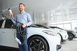 jovem homem comprando primeiro elétrico carro dentro a showroom. eco carro venda conceito foto