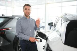 conceito do comprando elétrico veículo. bonito o negócio homem carrinhos perto elétrico carro às concessionária foto