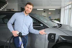 barba homem tentando uma Novo cobrando cabo com uma carro cobrando estação às a motor concessionária. conceito do comprando elétrico veículo. inteligente ecológico vivo foto