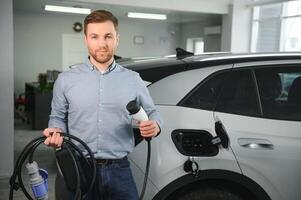 jovem homem comprando primeiro elétrico carro dentro a showroom. eco carro venda conceito foto