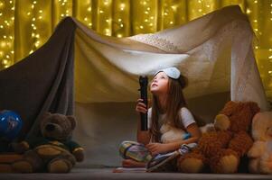 criança menina lendo com livro e lanterna e Urso de pelúcia Urso dentro barraca. antes indo para cama. foto