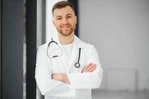 retrato do sorridente médico olhando às Câmera com braços cruzado dentro médico escritório foto