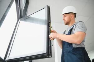 trabalhador dentro macacão instalando ou ajustando plástico janelas dentro a vivo quarto às casa foto