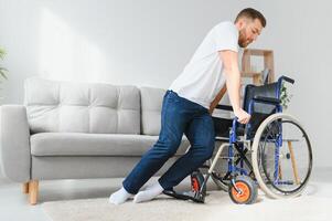 Desativado homem às casa tentativas para pegue para dele pés dentro uma cadeira de rodas. a conceito do reabilitação depois de lesões e carro acidentes. foto