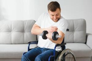 desportista sentado dentro cadeira de rodas e estendendo-se braços com halteres durante reabilitação exercício dentro moderno médico Centro. homem sentado em cadeira de rodas às casa foto