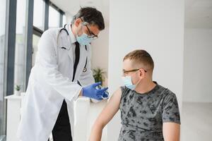 medicamento, vacinação e cuidados de saúde conceito - médico vestindo face protetora médico mascarar para proteção a partir de vírus doença com seringa fazendo injeção do vacina para masculino paciente. foto