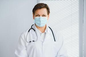 retrato do uma fêmea médico vestindo face mascarar e segurando dela paciente gráfico em digital tábua enquanto em pé às a hospital. foto