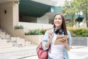 bela estudante mulher asiática com mochila e livros ao ar livre. menina sorriso feliz carregando um monte de livro no campus da faculdade. retrato feminino na universidade internacional da ásia. educação, estudo, escola foto