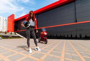 uma mulher posando com uma vibrante vermelho motocicleta. uma mulher em pé dentro frente do uma vermelho motocicleta foto