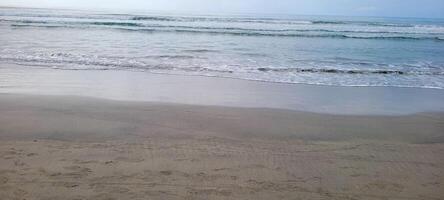 imagem do de praia com branco areia e calma mar em ensolarado dia com banhistas e surfistas em a de praia foto