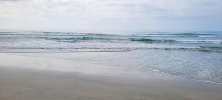 imagem do de praia com branco areia e calma mar em ensolarado dia com banhistas e surfistas em a de praia foto