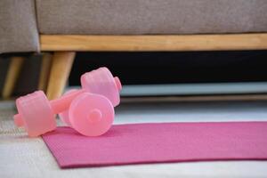 uma Rosa ioga esteira com dois Rosa colori halteres em isto. ginástica equipamento para casa exercício e flexibilidade treinamento. foto