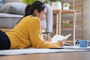 lindo jovem mulher dentro uma amarelo casual vestir desfrutando ouvindo para música e sorridente enquanto relaxante em a sofá às lar. jovem mulher com fones de ouvido usa computador portátil e Smartphone às lar. relaxar conceito foto