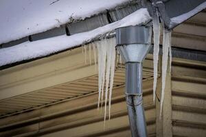 aço cano de esgoto com pingentes de gelo suspensão em amarelo construção cobertura canto em inverno maçante dia foto