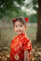 alegre jovem menina com adorável vermelho cabelo pães vestindo uma vibrante tradicional chinês cheongsam vestir ao ar livre dentro a jardim parque. chinês dia conceito. foto