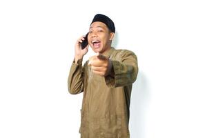 animado ásia muçulmano masculino apontando às Câmera enquanto falando usando Móvel telefone isolado em branco fundo foto
