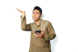 confuso ásia muçulmano homem vestindo islâmico roupas apresentando para acima com segurando Móvel telefone isolado em branco fundo foto