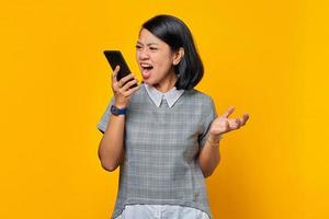 retrato de mulher asiática zangada quando fala no smartphone sobre fundo amarelo foto