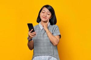 Retrato de uma jovem asiática sorridente, pensando na pergunta com o dedo no queixo e segurando um telefone celular foto