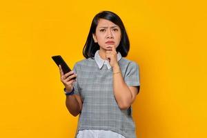 retrato de uma jovem mulher asiática pensando em algo e segurando o telefone celular sobre o fundo azul foto