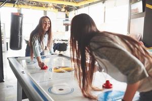 duas lindas gêmeas jogam air hockey na sala de jogos e se divertem foto