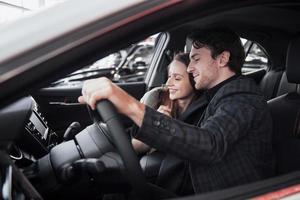 tomar sua decisão. lindo casal apaixonado, sentado em um carro novo junto na concessionária, homem bonito e sua namorada apaixonada escolhendo um carro juntos, veículo de consumismo foto