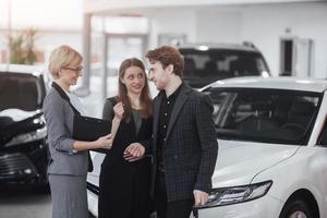 comprando seu primeiro carro juntos. visão de alto ângulo de um jovem vendedor de carros na concessionária contando aos clientes sobre as características do carro foto