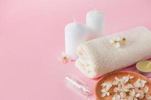 produtos cosméticos naturais para spa e aromaterapia. conceito de relaxamento. velas, flores e uma toalha em um fundo rosa. foto