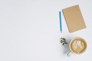 caderno fechado lápis colorido deixa xícara de café com fundo branco latte art. conceito de foto bonita de alta qualidade