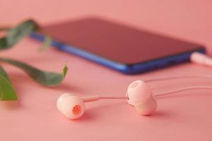 telefone inteligente com tela vazia, fone de ouvido no fundo rosa foto