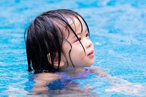tiro na cabeça da menina na piscina azul. tempo relaxante. temporada de verão. criança feliz brincando de natação parque aquático. criança de 4-5 anos. foto