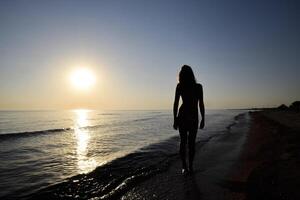 silhueta do uma menina contra a pôr do sol de a mar foto