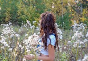 menina com grandes ondulado cabelo dentro uma compensação com fofo sementes do plantas. plantas com fofo sementes. foto