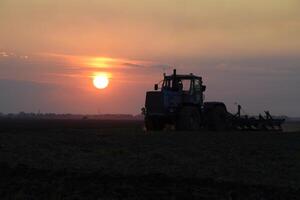 trator aração arado a campo em uma fundo pôr do sol. trator silhueta em pôr do sol fundo foto