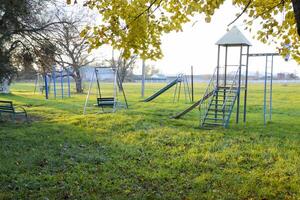 crianças Parque infantil perto a estádio em a fundo do pôr do sol. balanços, deslizar e escada. carrossel e fazer compras. lazer para crianças. crianças Parque infantil. balanços e uma deslizar para deslizar foto