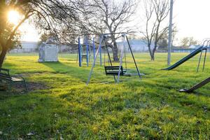 crianças Parque infantil perto a estádio em a fundo do pôr do sol. balanços, deslizar e escada. carrossel e fazer compras. lazer para crianças. crianças Parque infantil. balanços e uma deslizar para deslizar foto