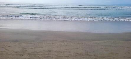 imagem do de praia com branco areia e calma mar em ensolarado dia com banhistas e surfistas em a de praia foto