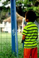 pequeno criança em a margem visto a partir de atrás olhando para dentro a futebol campo foto