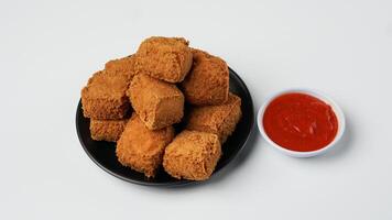 frito tofu em uma Preto prato com Pimenta molho em uma branco fundo foto