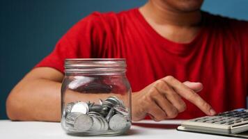 homem com moedas dentro uma Claro transparente vidro jar. salvando dinheiro conceito foto
