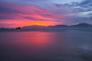 pôr do sol em a de praia com Laranja vermelha céu refletido em molhado areias. cênico Visão do pôr do sol dentro banyuwangi, Indonésia foto