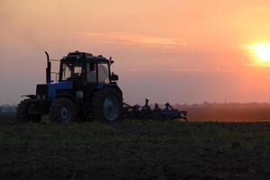 trator aração arado a campo em uma fundo pôr do sol. trator silhueta em pôr do sol fundo foto