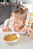 fofa bebê menina criança pequena sentado dentro a Alto cadeira e comendo dela almoço sopa às casa cozinha. foto