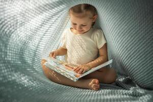 pequeno menina desfrutando do Reveja uma livro debaixo azul tricotado xadrez dentro ensolarado manhã foto